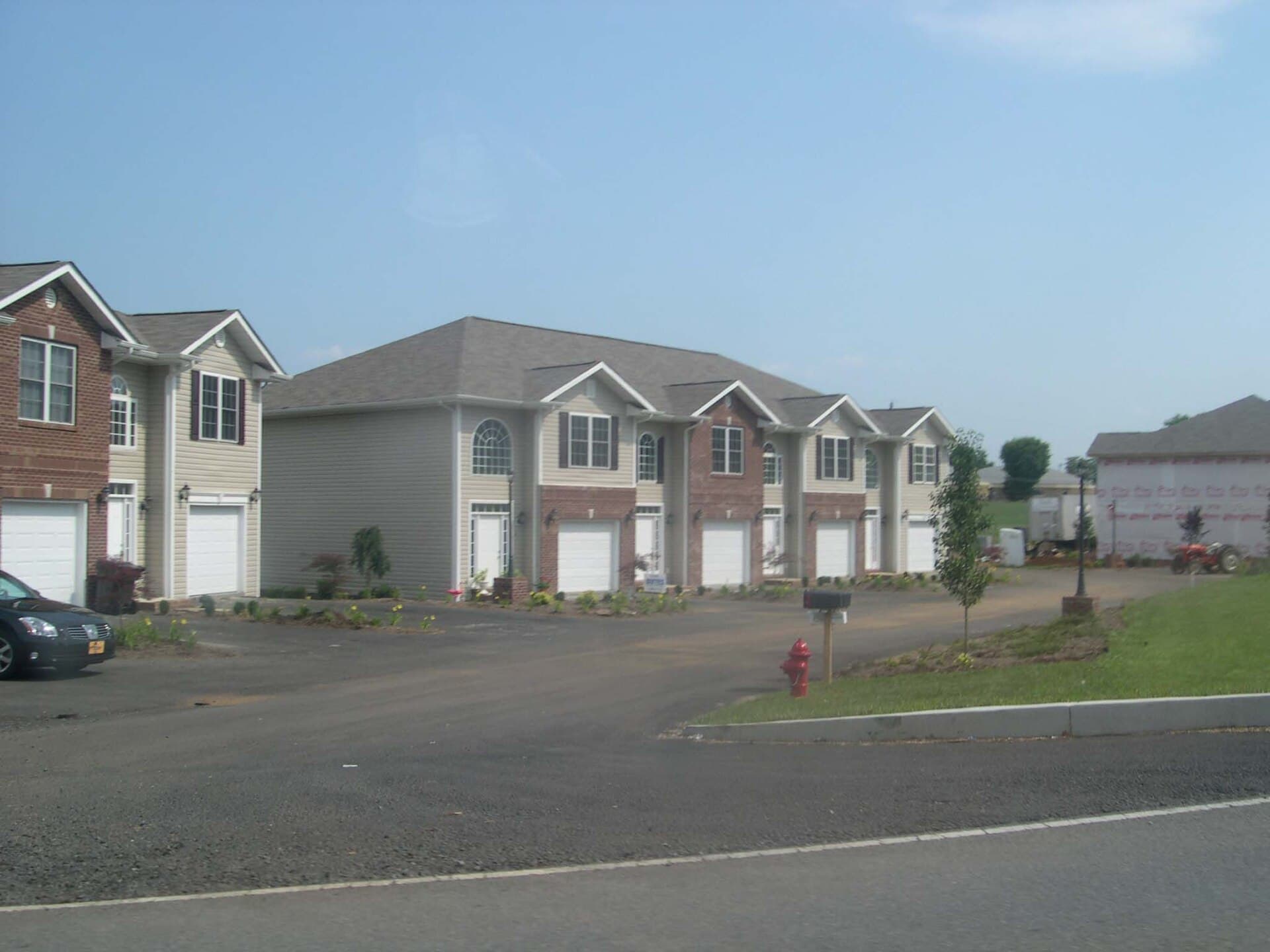 Attached townhouses with garage-dominated facades facing a wide asphalt court, a fire hydrant and a mailbox at the kerb