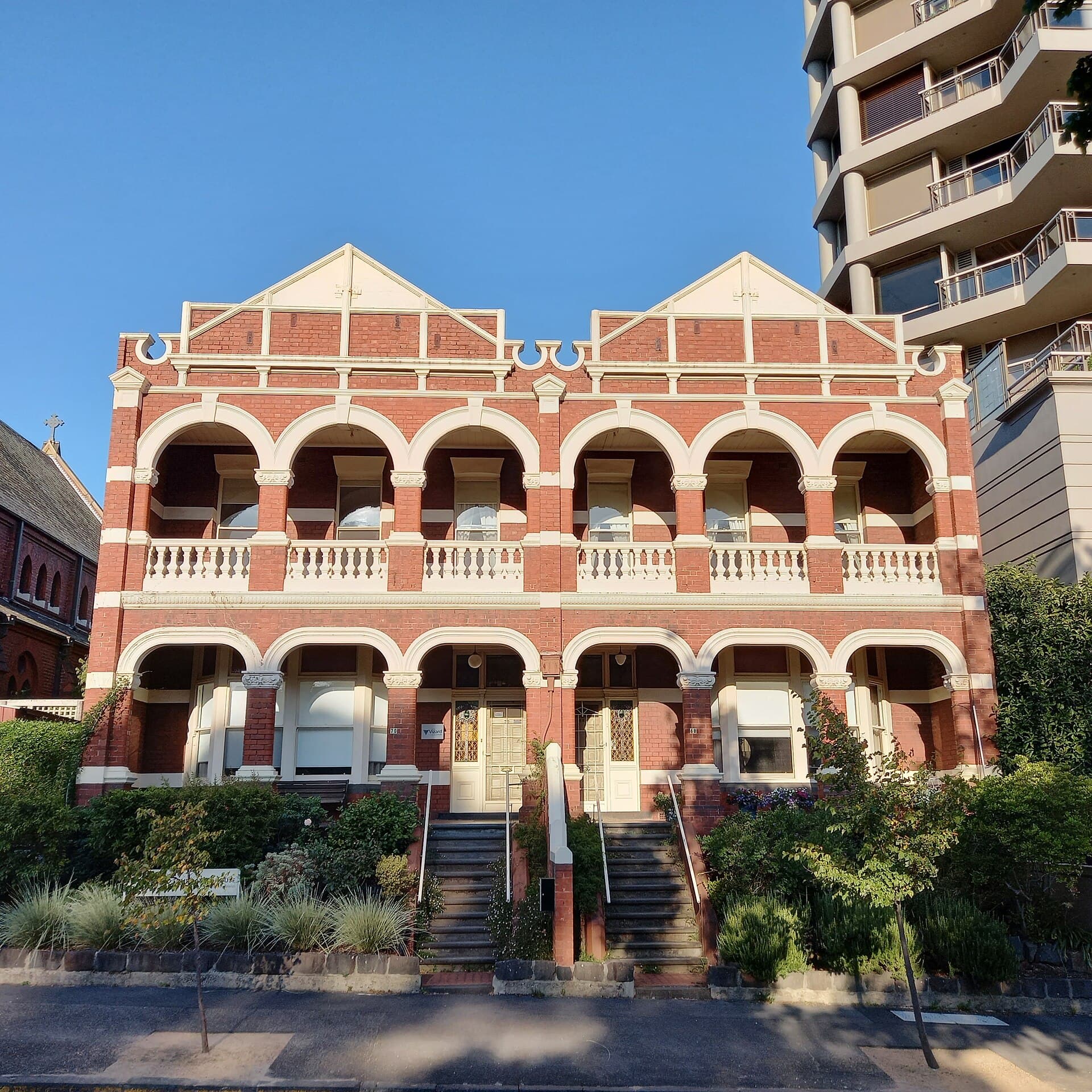 Two-storey red-brick terrace with arched verandahs standing beside a taller contemporary apartment building